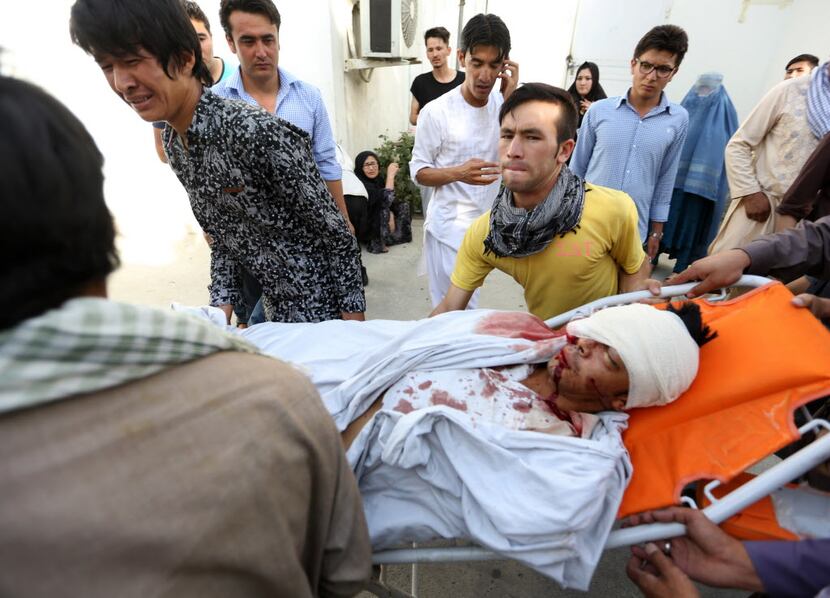 Afghans help a man who was injured in a deadly explosion that struck a protest march by...