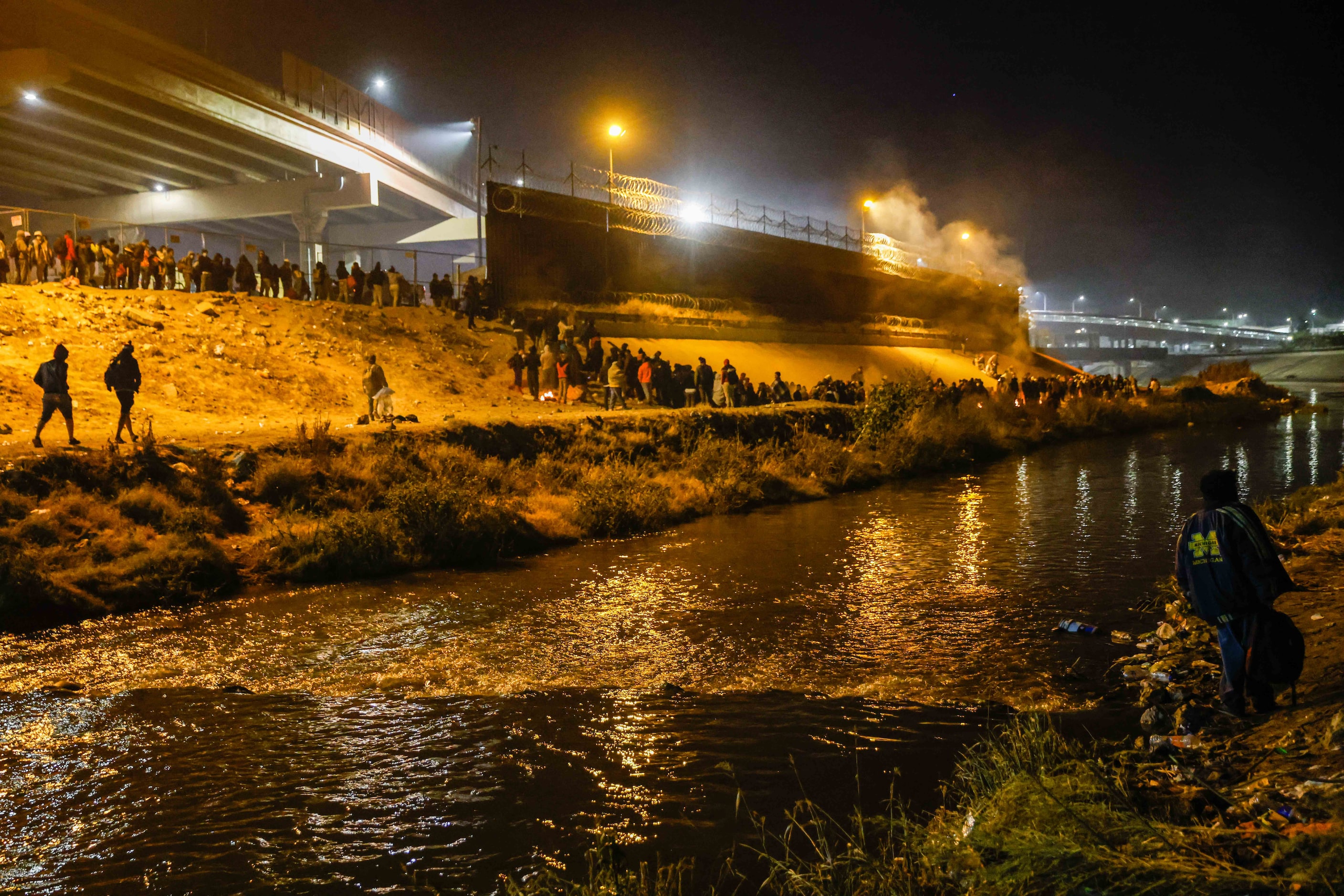 Migrants wait in line along a border wall in El Paso, Texas after crossing the Rio Grande...