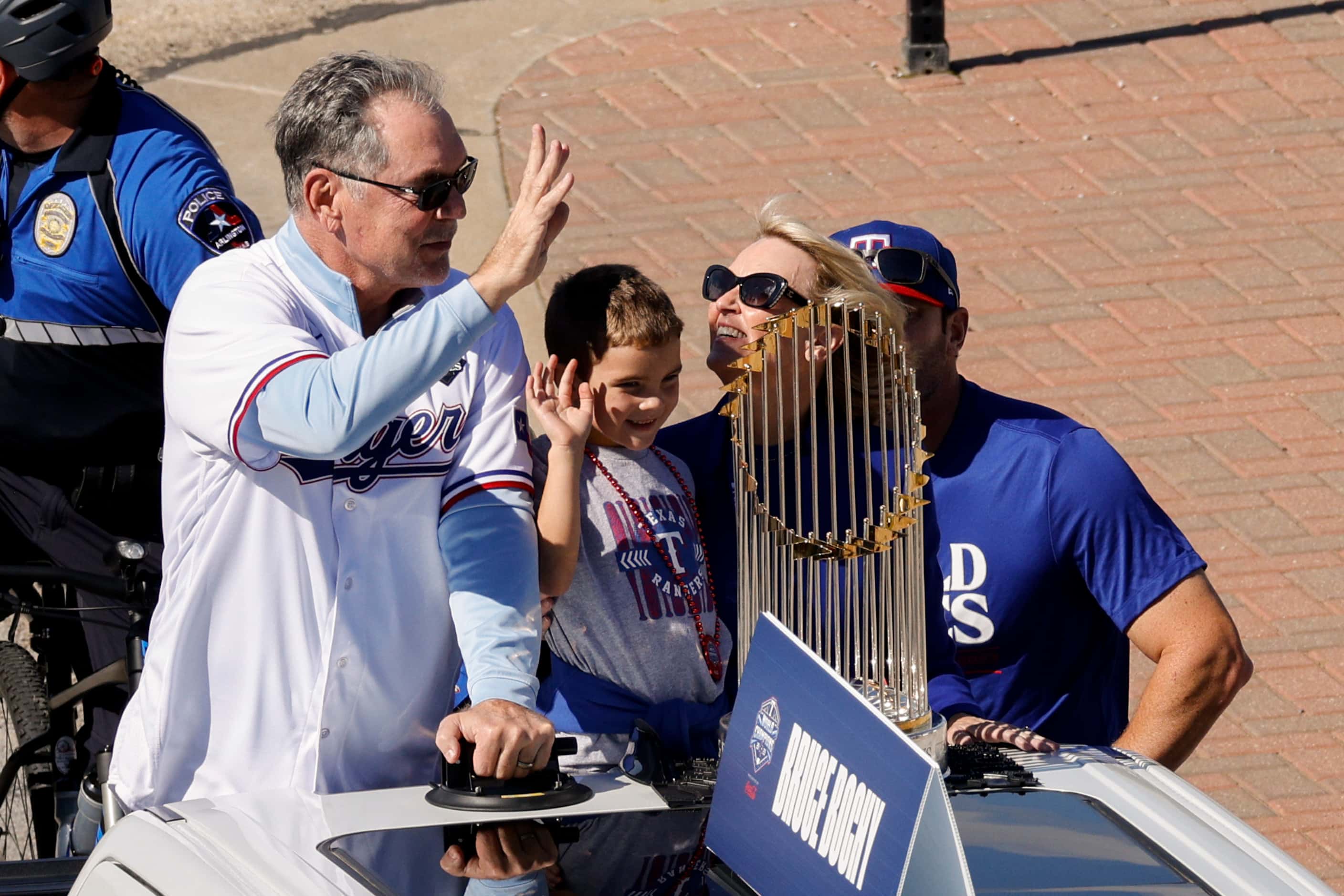 Texas Rangers manager Bruce Bochy waves to the crowd alongside the Commissioner’s Trophy...