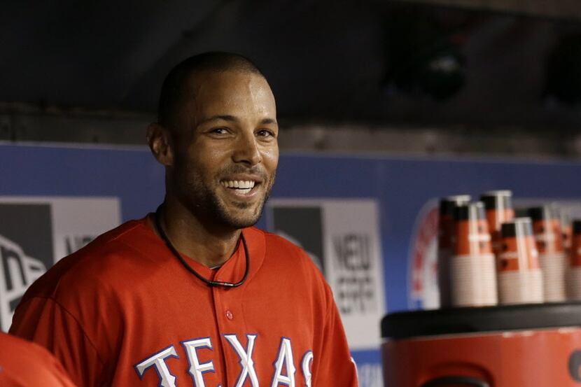 Texas Rangers' Alex Rios (51) smiles as he sits in the dugout after scoring on a sacrifice...