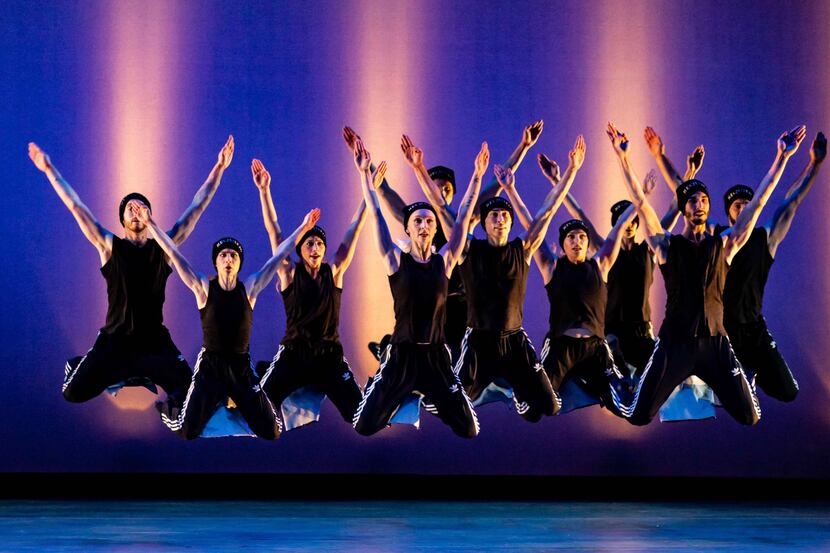 A group of dancers dressed in black jump at the same time on stage.