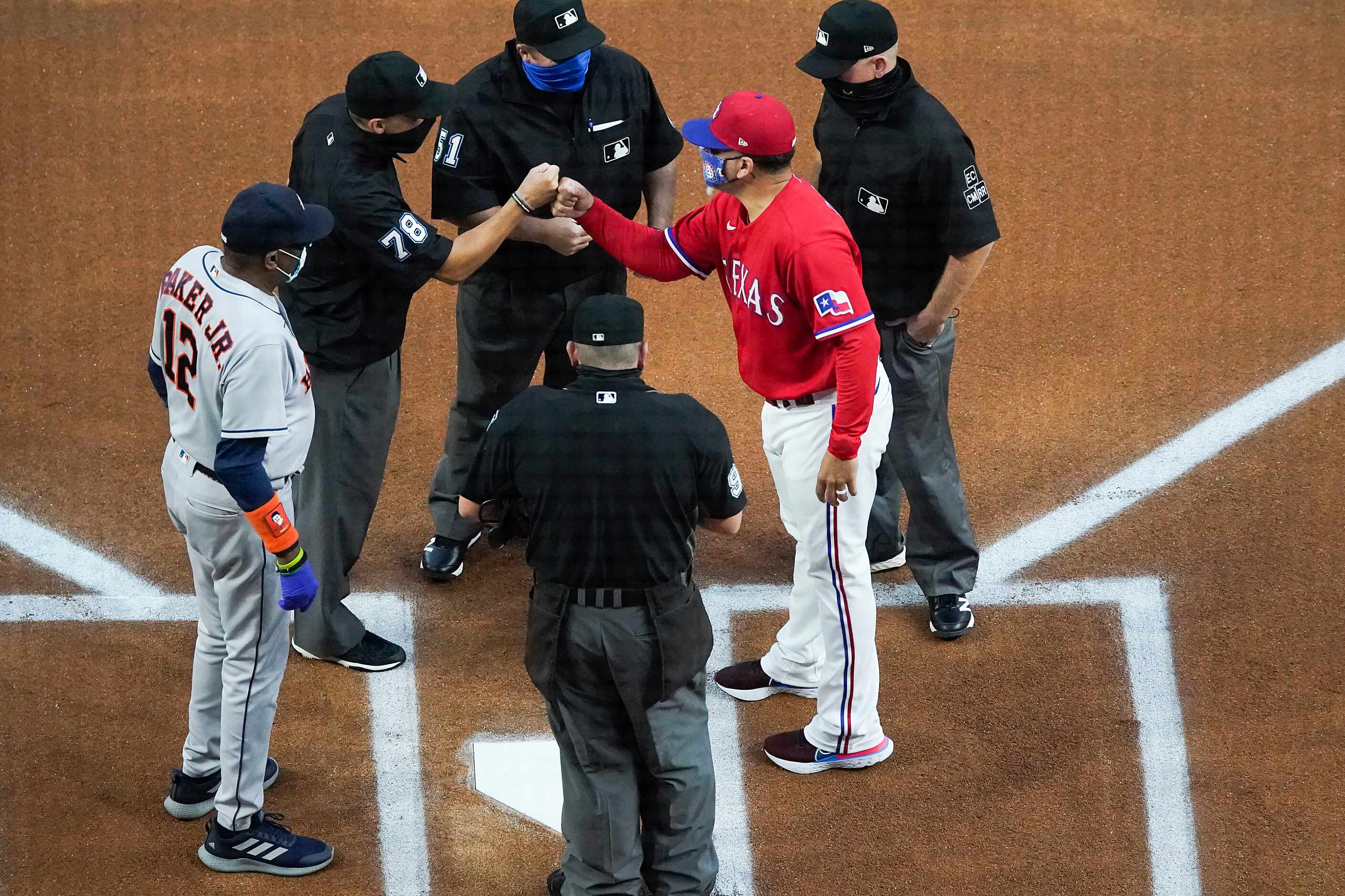 Texas Rangers coach Hector Ortiz fist bumps umpire Adam Hamari as he meets with Houston...
