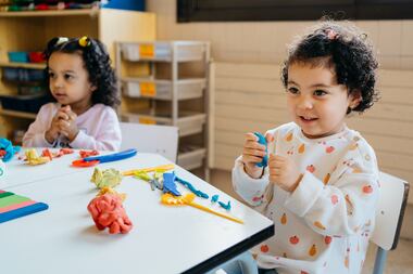 Cute multiracial toddlers sit at a table and play with modeling clay in a kindergarten...