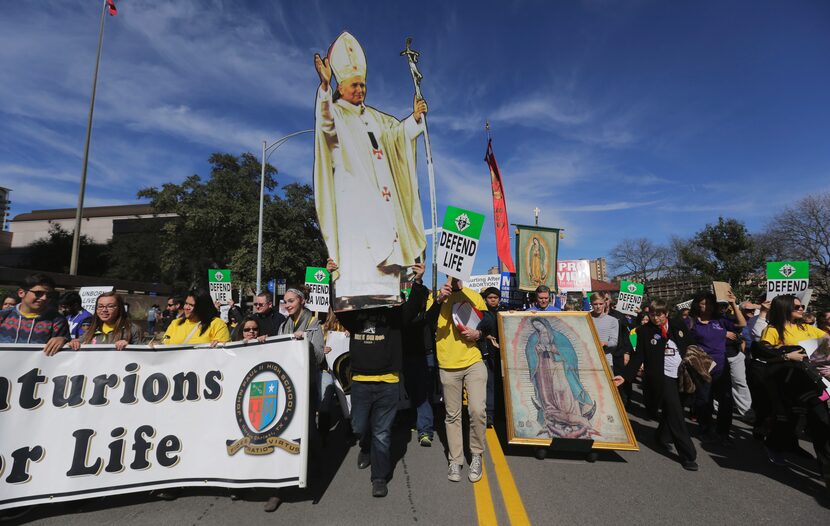 Anti-abortion supporters carry signs and a life-sized photo of Pope John Paul II as they...