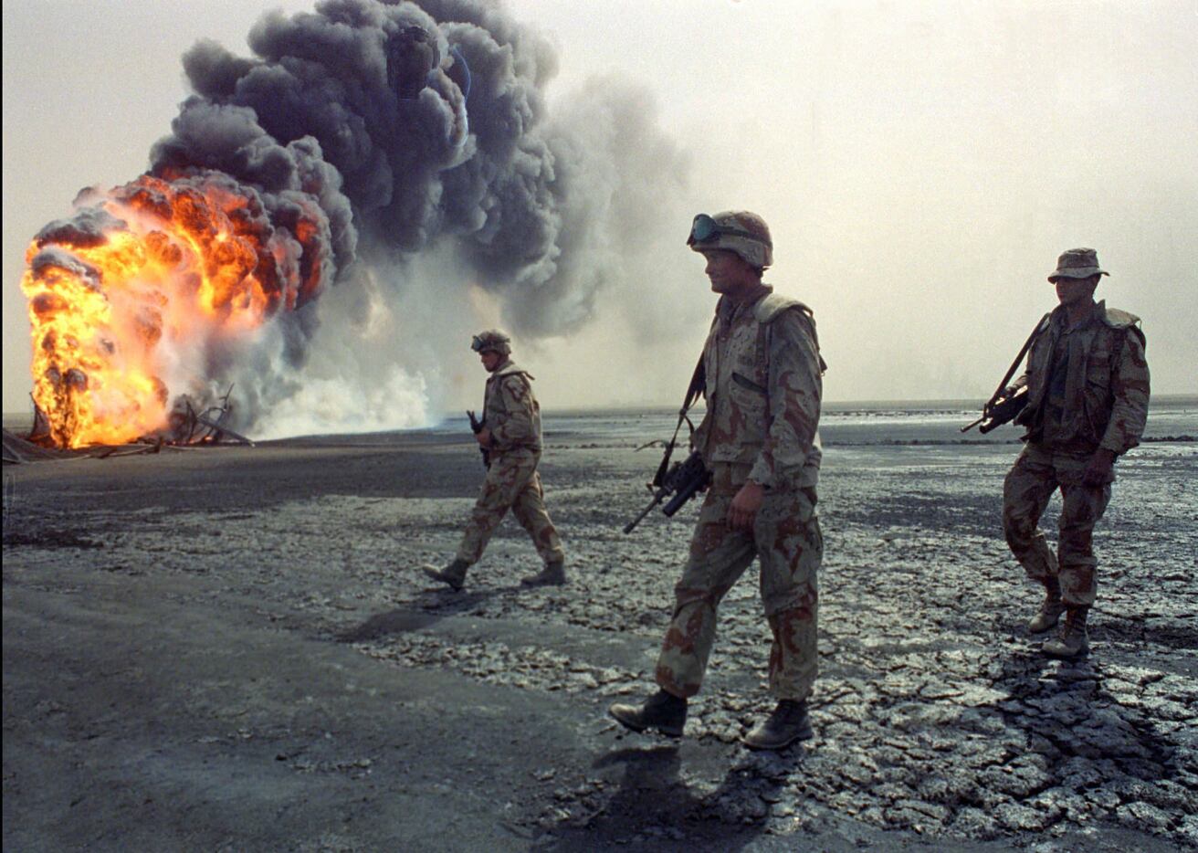 A U.S. Marine patrol walks across the charred oil landscape near a burning well  during...
