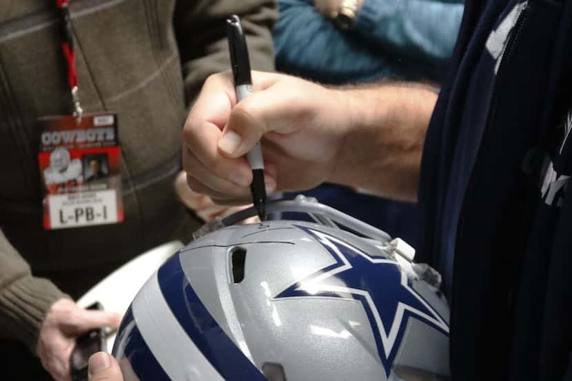 Dallas Cowboys quarterback Tony Romo signs a helmet as he talks to the news media at Dallas...