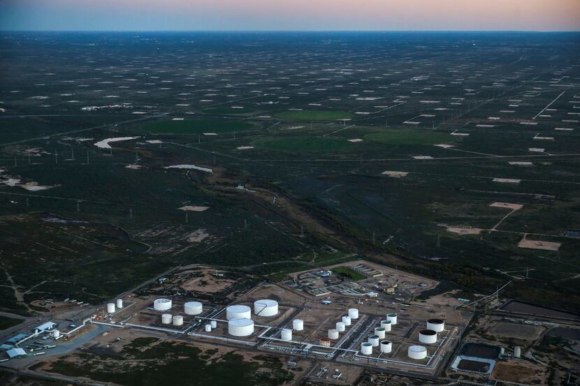 An oil tank farm is seen in the foreground of a pumpjack speckled production field, just...