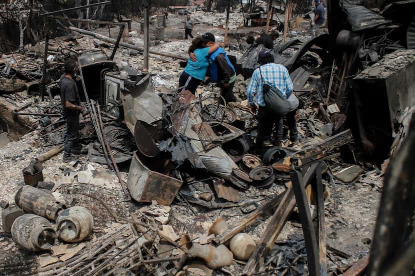 ARCHIVO - Residentes se abrazan entre los escombros y las casas quemadas por incendios...