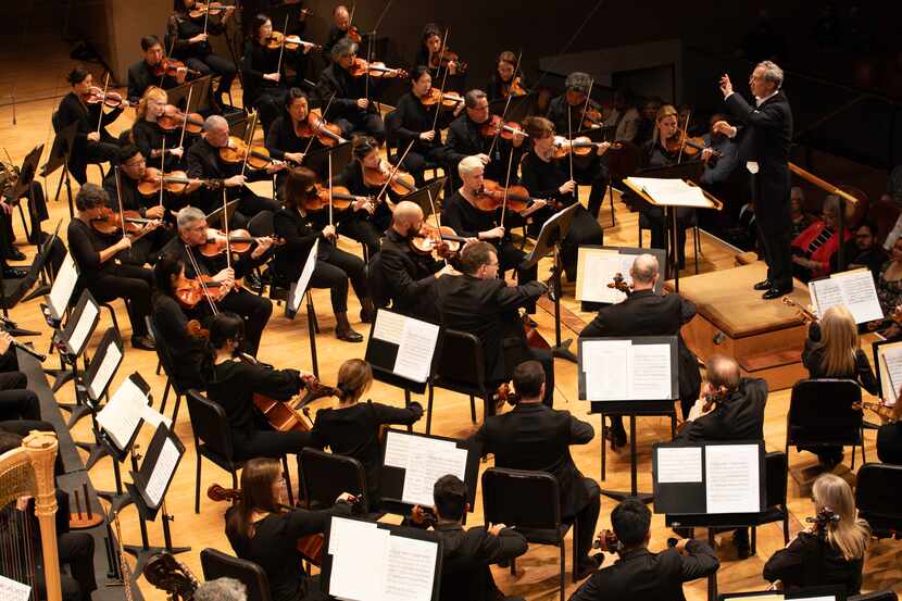 Musical conductor stands in front of performing orchestra musicians.