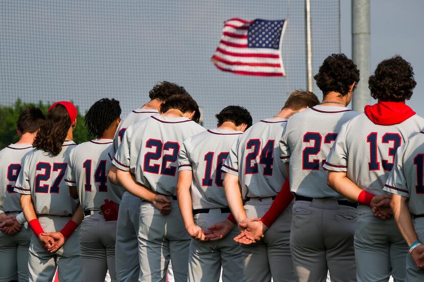 Below a half-staff flag, Allen players bow their heads during a moment of silence for...