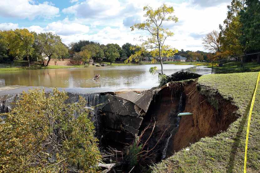 Parts of a backyard are washed away at the Prestonwood Lake dam in northwest Arlington,...