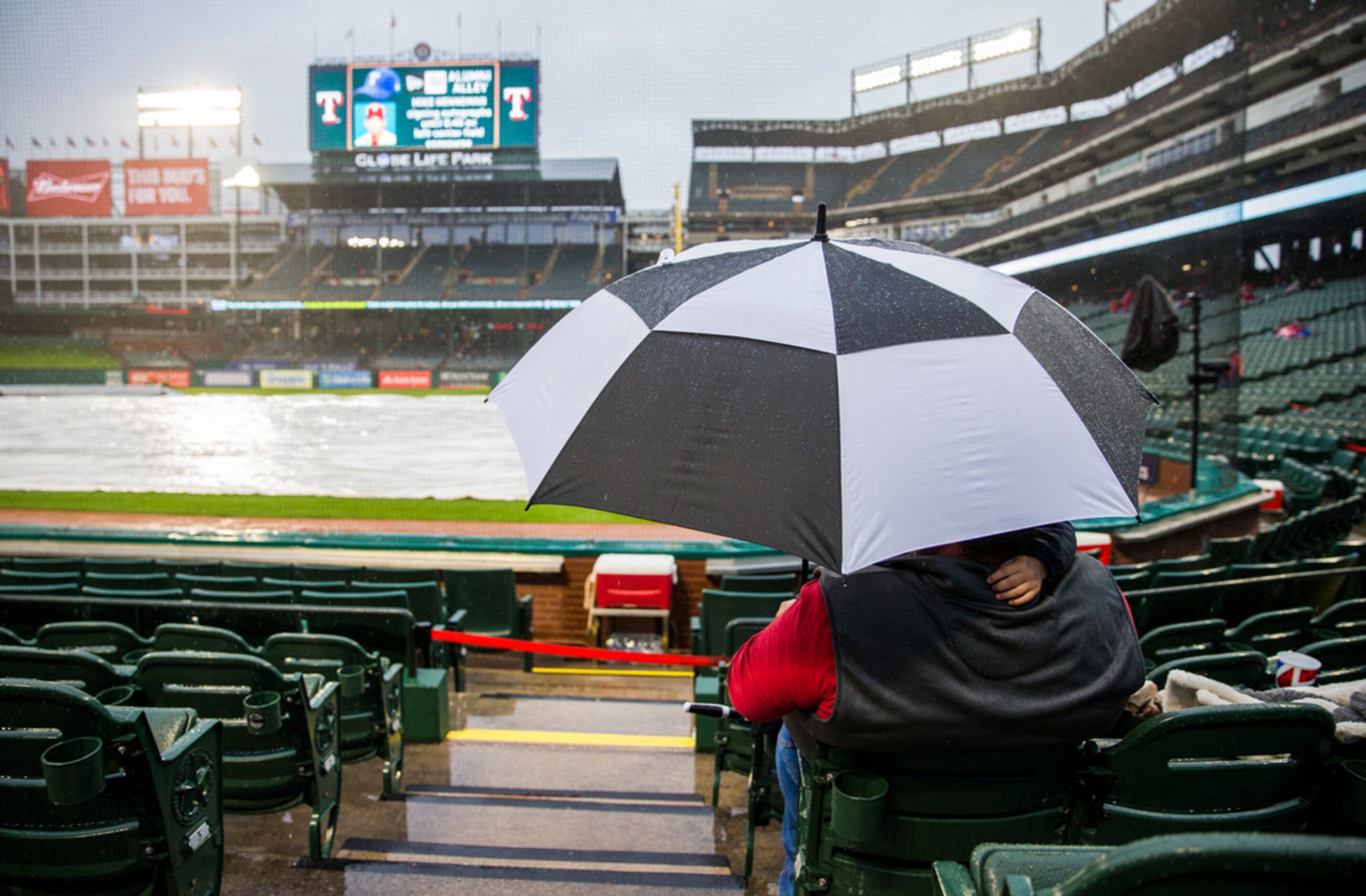 Chris Dickson and his grandson wait in the rain before an MLB game between the Texas Rangers...