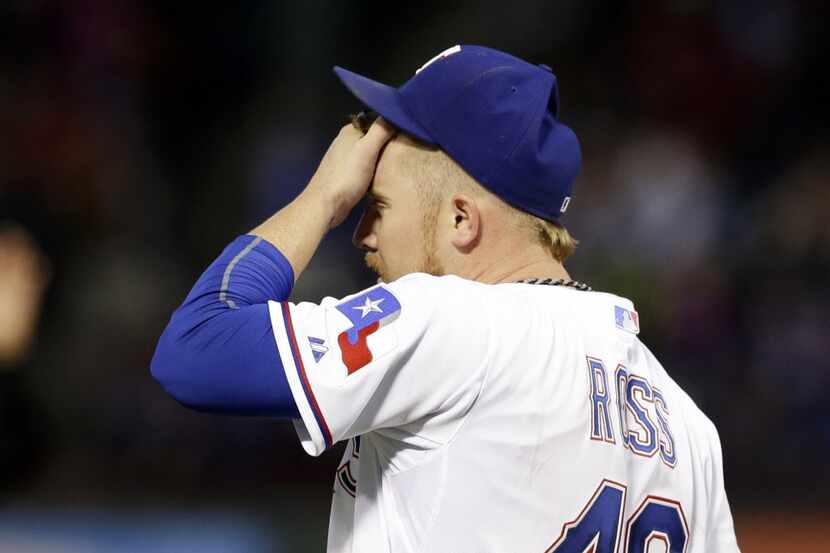 Texas Rangers starting pitcher Robbie Ross wipes his forehead after giving up a double to...