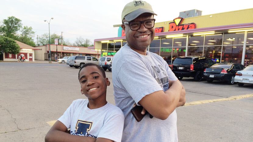 A little brother and a big brother stand back to back in front of a pizza restaurant.