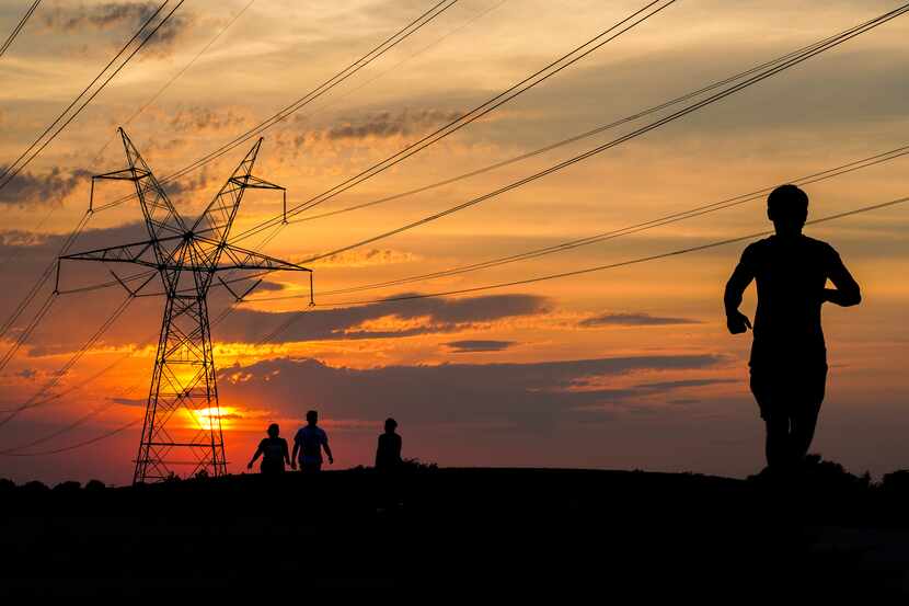 People walk and run along the Bluebonnet Trail as the sun sets behind electric transmission...