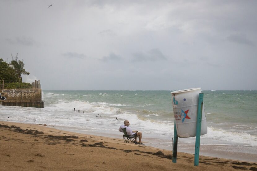 A man sits in front of a beach watching as the waves break before the arrival of Tropical...