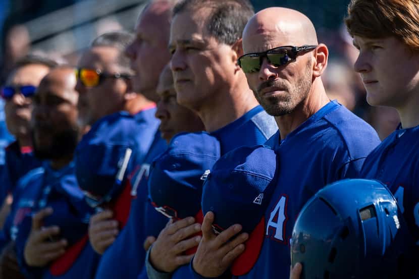 Texas Rangers manager Chris Woodward stands for the national anthem before a spring training...