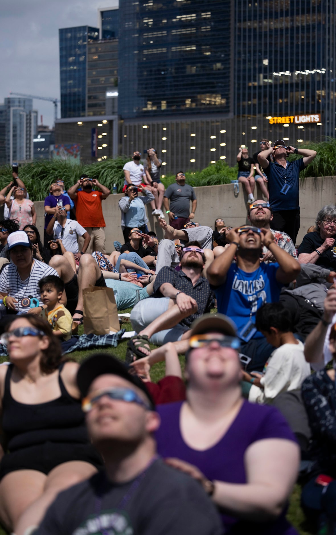 People watch the eclipse enter totality as building lights turn on behind them during the...