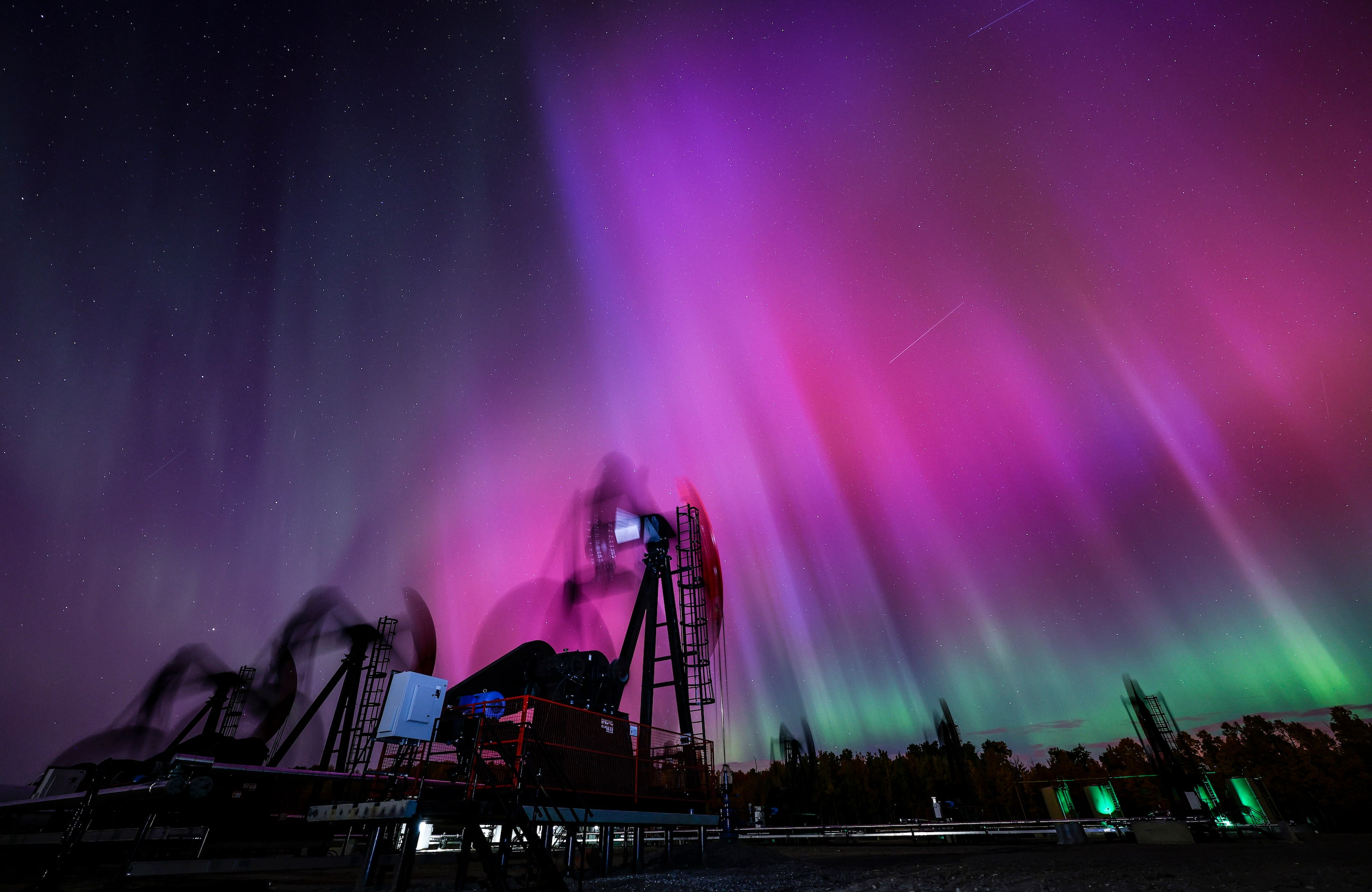 An aurora borealis makes an appearance over pumpjacks as they draw out oil and gas from well...