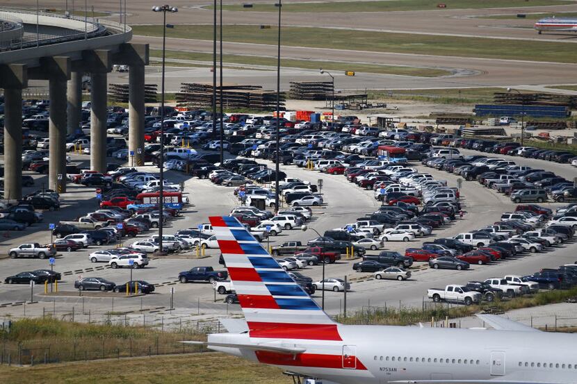 An American Airlines jet tail and travelers' cars in a parking lot at DFW International...