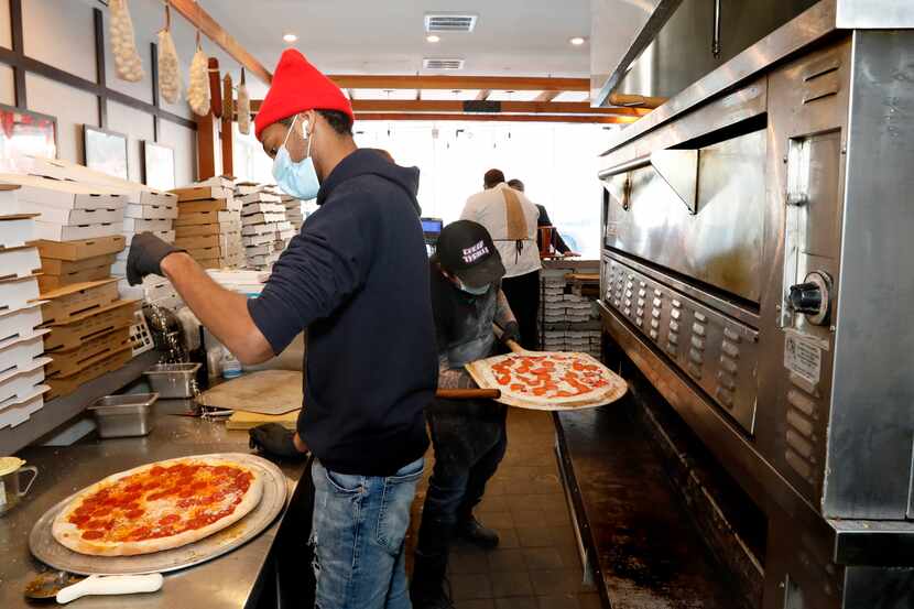 Jalen Holloway, left, puts cheese on a pizza as Jacob Walker, right, puts a pepperoni pizza...