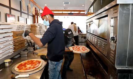 Jalen Holloway, left, puts cheese on a pizza as Jacob Walker, right, puts a pie in the oven...