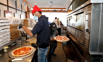 Jalen Holloway, left, puts cheese on a pizza as Jacob Walker, right, puts a pie in the oven...