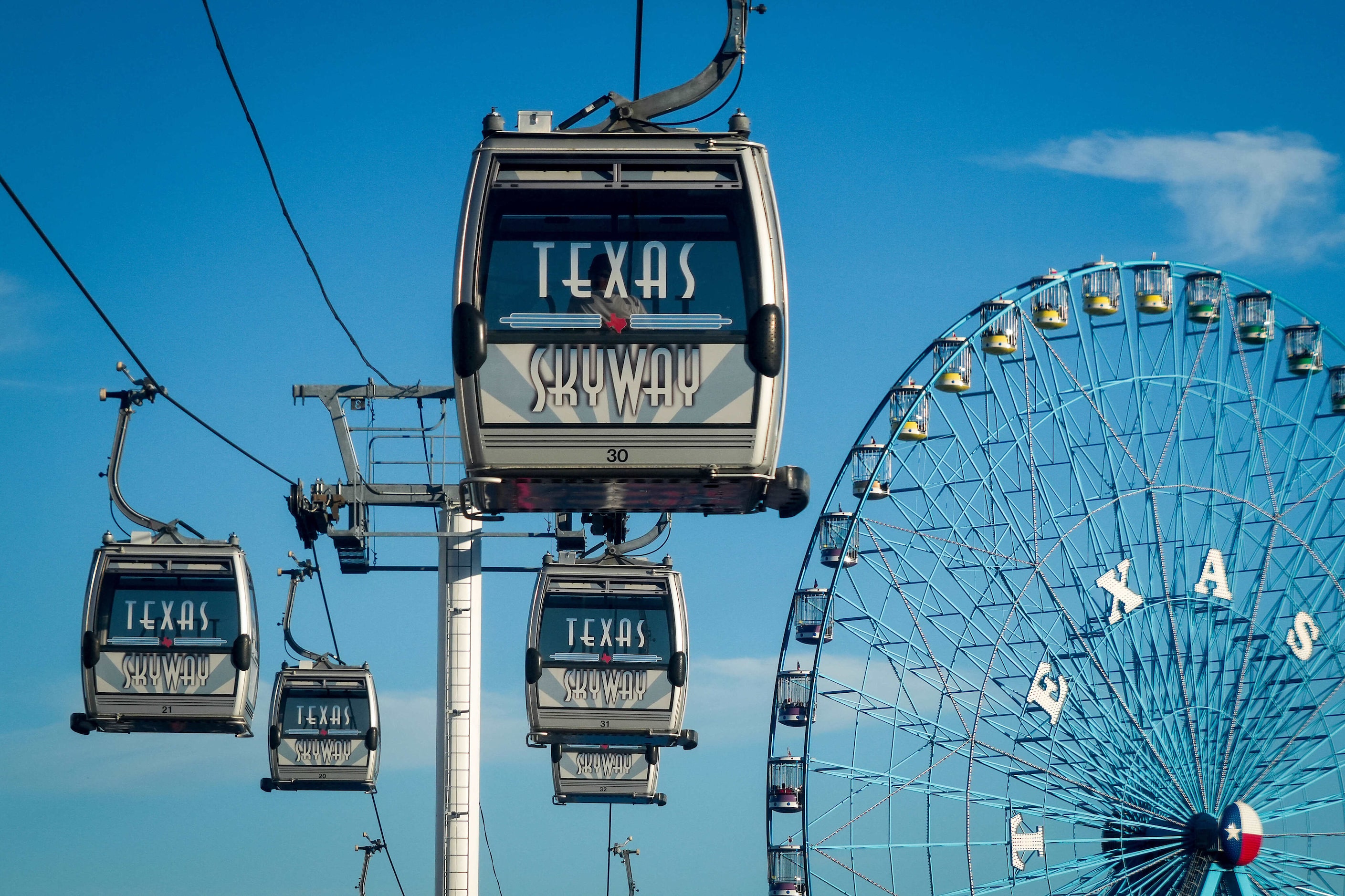 Fairgoers ride the Texas Skyway over the midway past the Texas Star Ferris wheel at the...