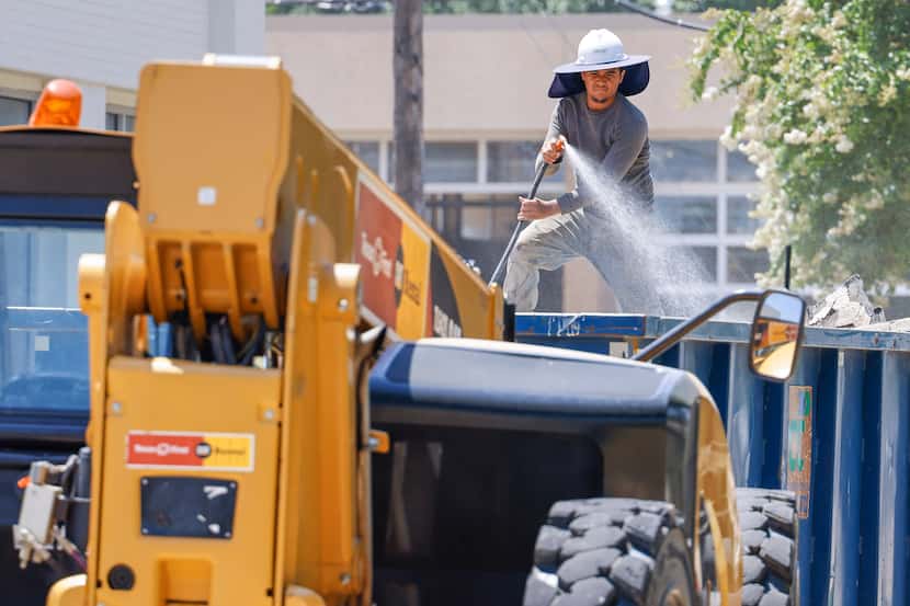 Construction worker Jorge Aguilera (right) hose water over the dust collected from debris on...