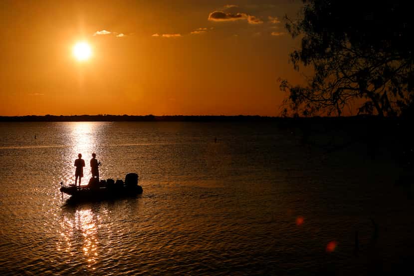 A couple fishes along the shoreline of Joe Pool Lake near sunset at Cedar Hill State Park in...