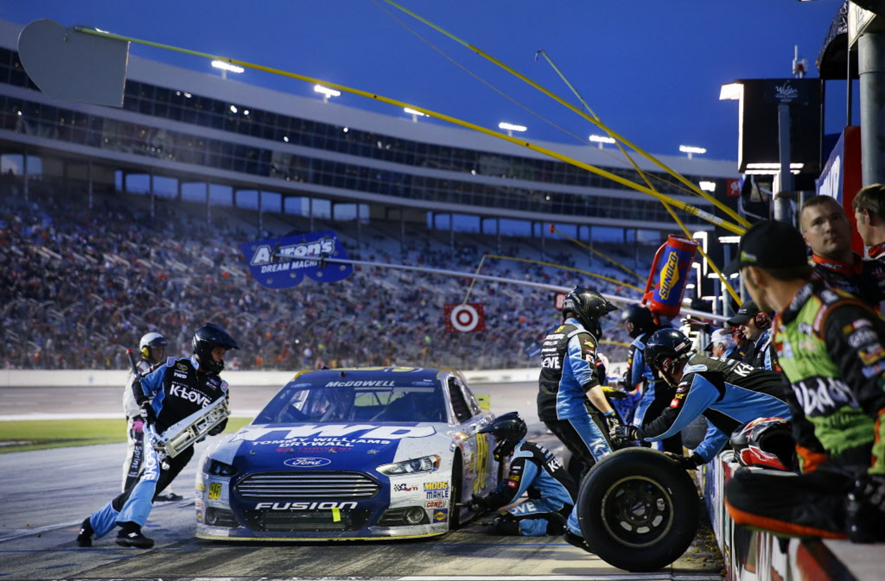 Sprint Cup Series driver Michael McDowell (95) receives a four-tire change as twilight falls...