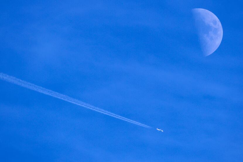 Contrails form behind a commercial jet passingby the moon over Dallas, November 30, 2022. 
