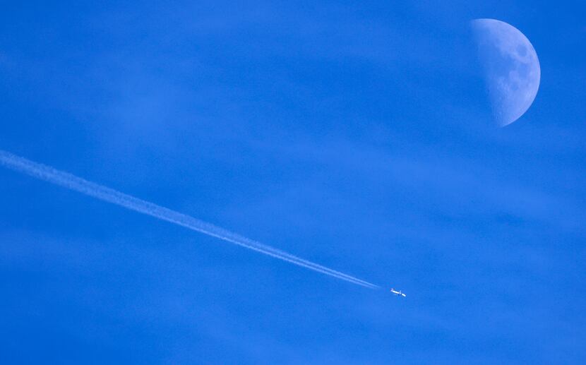 Contrails form behind a commercial jet passing by the moon over Dallas.