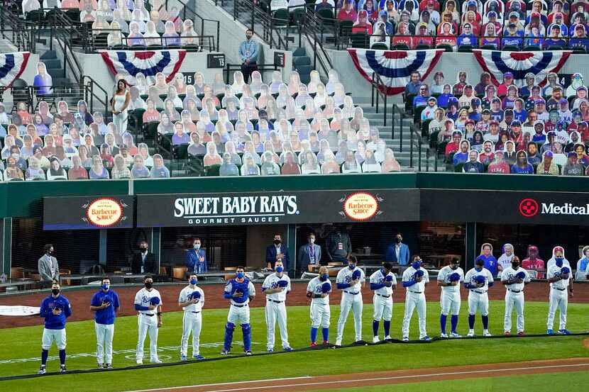 In front of a sea of cutout photos, , Texas Rangers players stand during the singing of the...