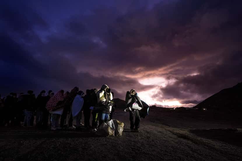 Solicitantes de asilo se cubren con frazadas mientras hacen fila en un campamento...