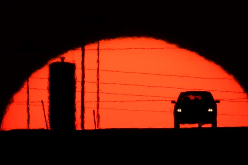 A car is silhouetted against the setting sun as it travels along Interstate 70 in Kansas...