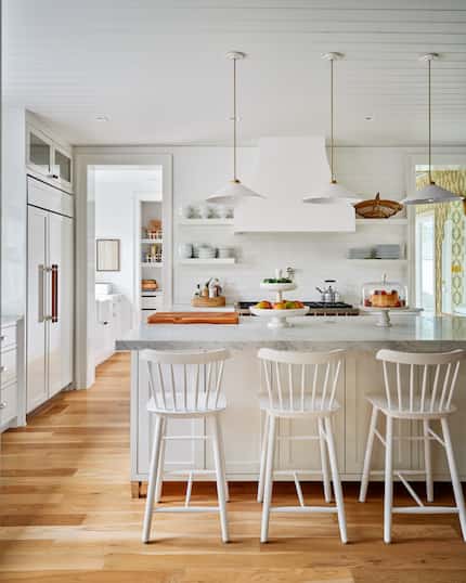 A kitchen has counter-height stools at the countertop, open shelving near the stove and...