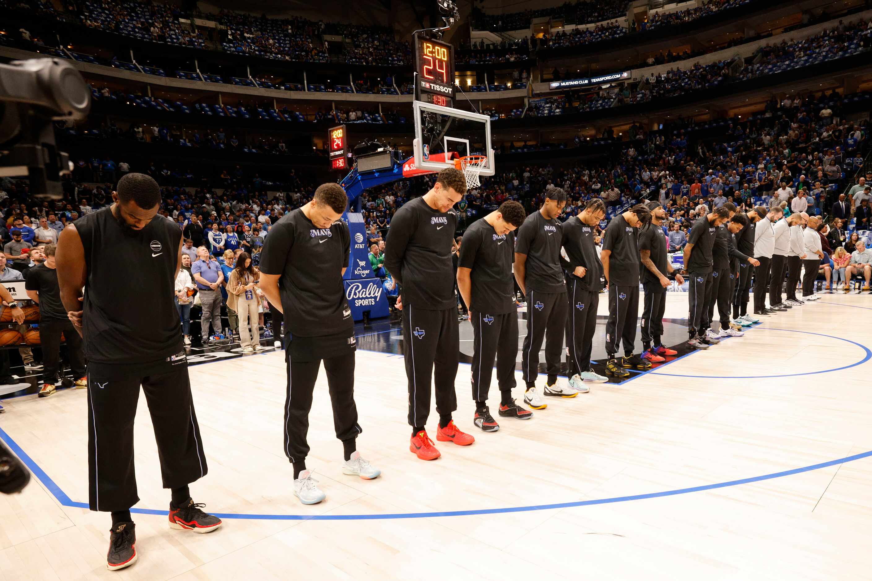 Dallas Mavericks players stand during a moment of silence for Kathy Drysdale, the mother of...