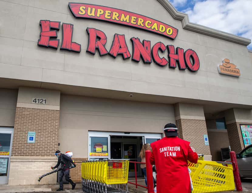 Jorge Osorio (right) sanitizes shopping carts as another employee power washes the exterior...