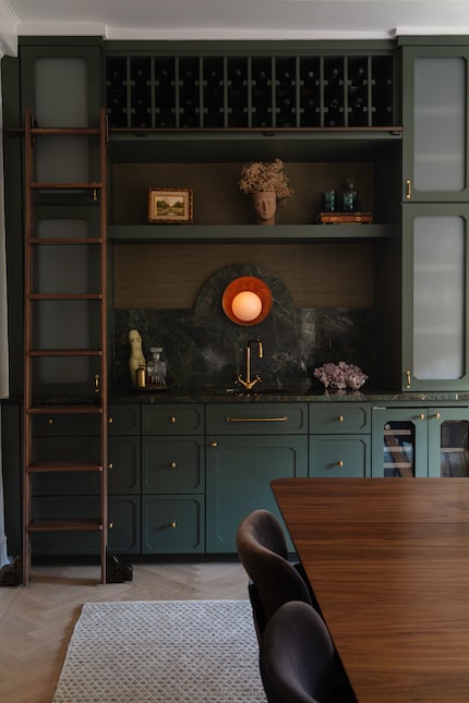 Dark green home bar with antique light and a dining table in the foreground