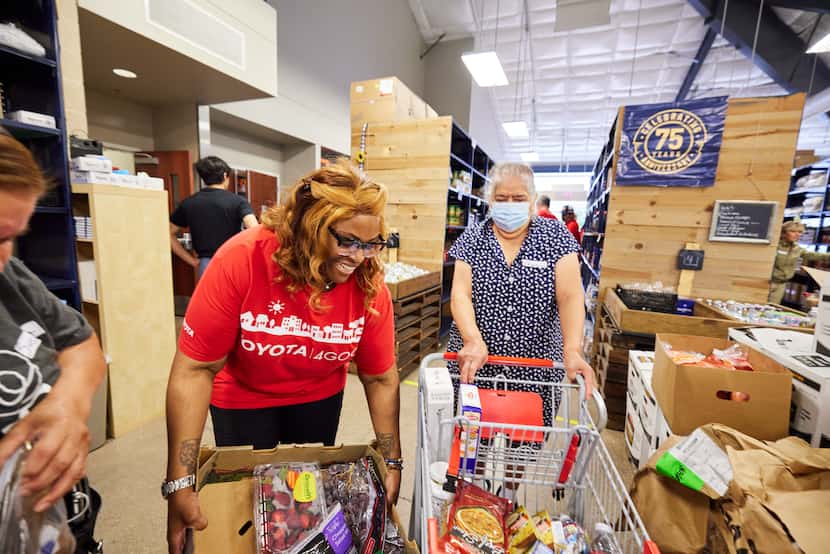 Woman in red volunteer T-shirt assists woman pushing a grocery cart through the food aisles...