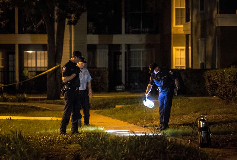 Lewisville police officers clean blood stains from the pavement at Oak Forest Apartments in...