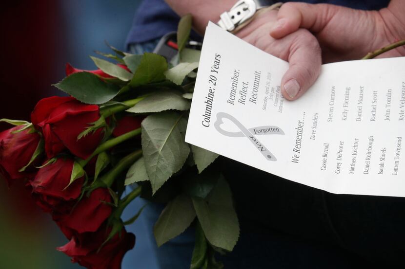 A woman holds a bouquet of roses and a program bearing the names of the victims of the...