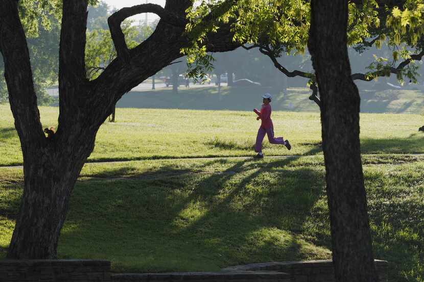 After days of rainy weather a jogger is framed by trees as she runs in Lake Cliff Park on a...