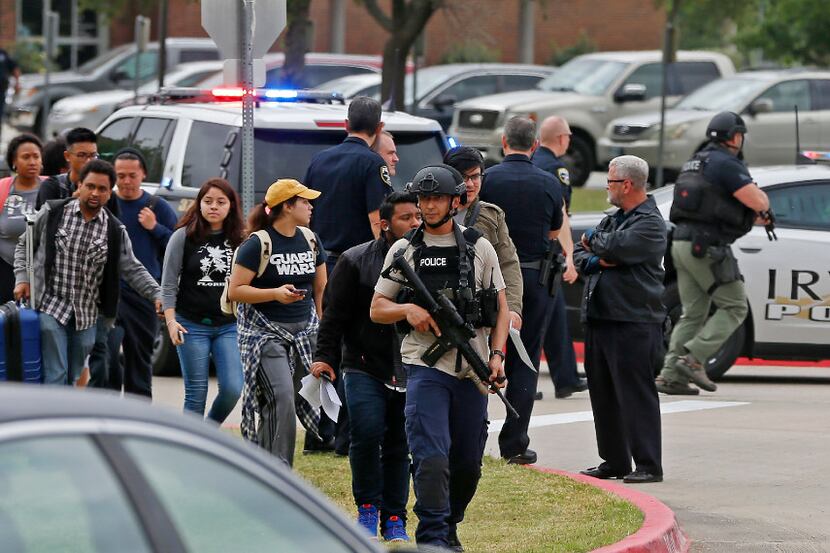 An officer leads a group of students walking out of the building as Irving police officers...