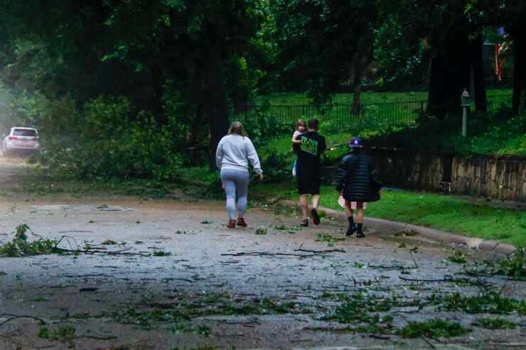 A family walks along a street littered with downed tree branches after a tornado-warned...