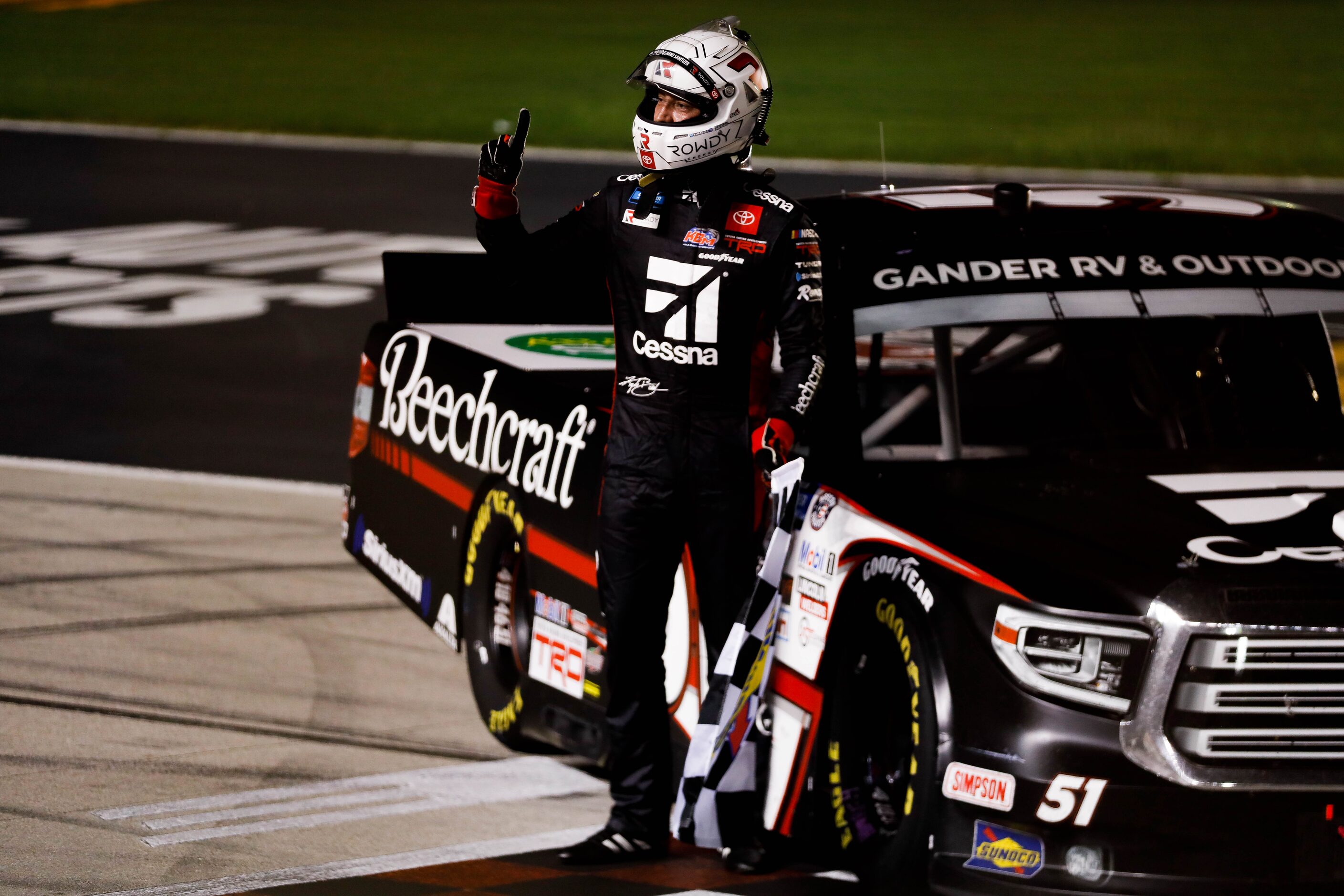 Driver Kyle Busch (No. 51) holds the race flag after winning the Vankor 350 NASCAR Gander RV...