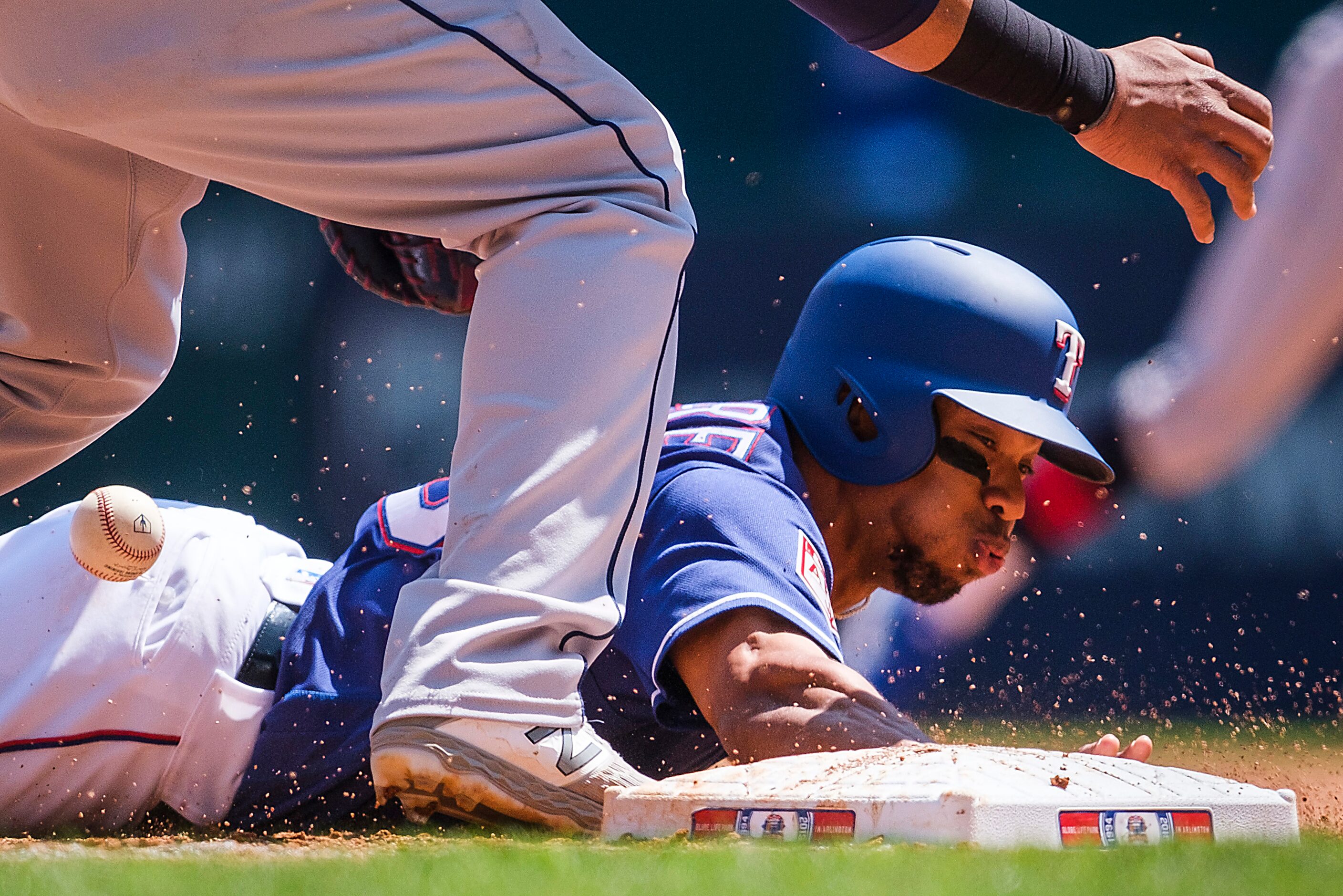 Texas Rangers outfielder Ben Revere dives back to first base as the ball gets away from...