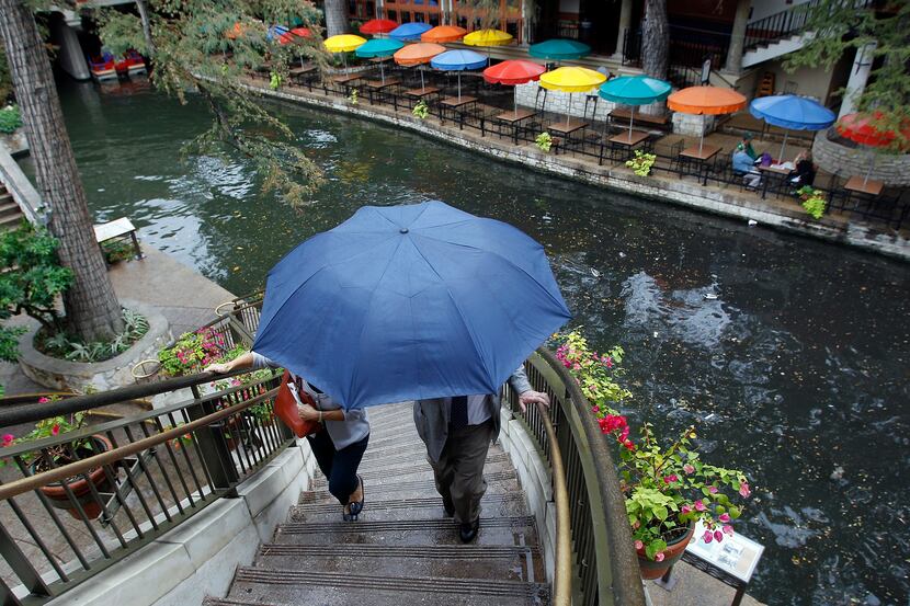 Visitors use an umbrella for protection from a light rain as they walk along the River Walk,...