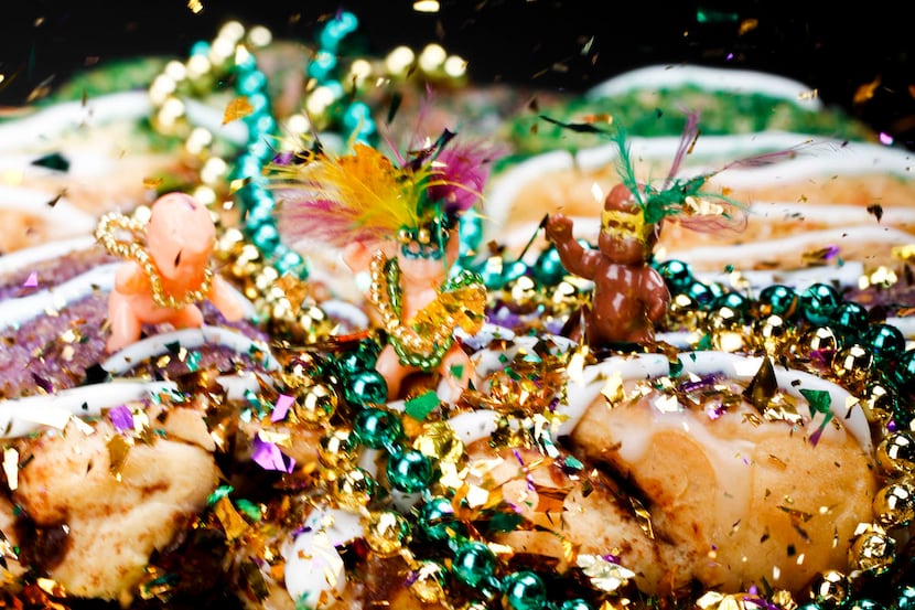 Decorated Mardi Gras babies stand atop a king cake with beads and confetti.